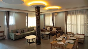 A modern living room with a sofa, dining table set for four, and a decorative pillar. - Sumix Hotel (Entebbe)