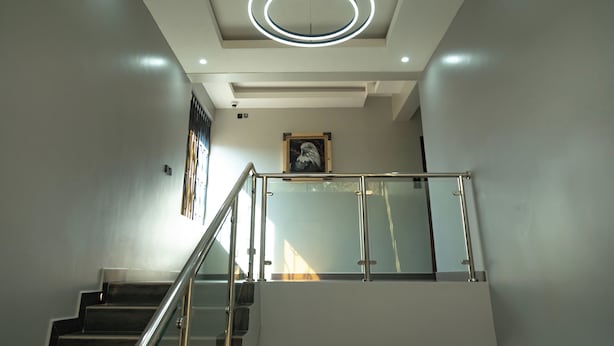 A modern staircase with glass railings and a circular light fixture on the ceiling. - Sumix Hotel (Entebbe)