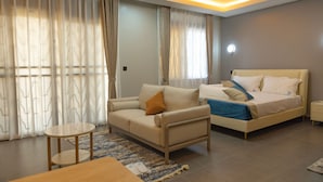 A modern hotel room with a sofa, a bed, a small table, and a rug. - Sumix Hotel (Entebbe)