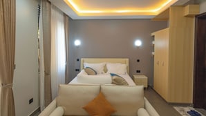 A modern hotel room with a large bed, bedside tables, a wardrobe, and a seating area. - Sumix Hotel (Entebbe)