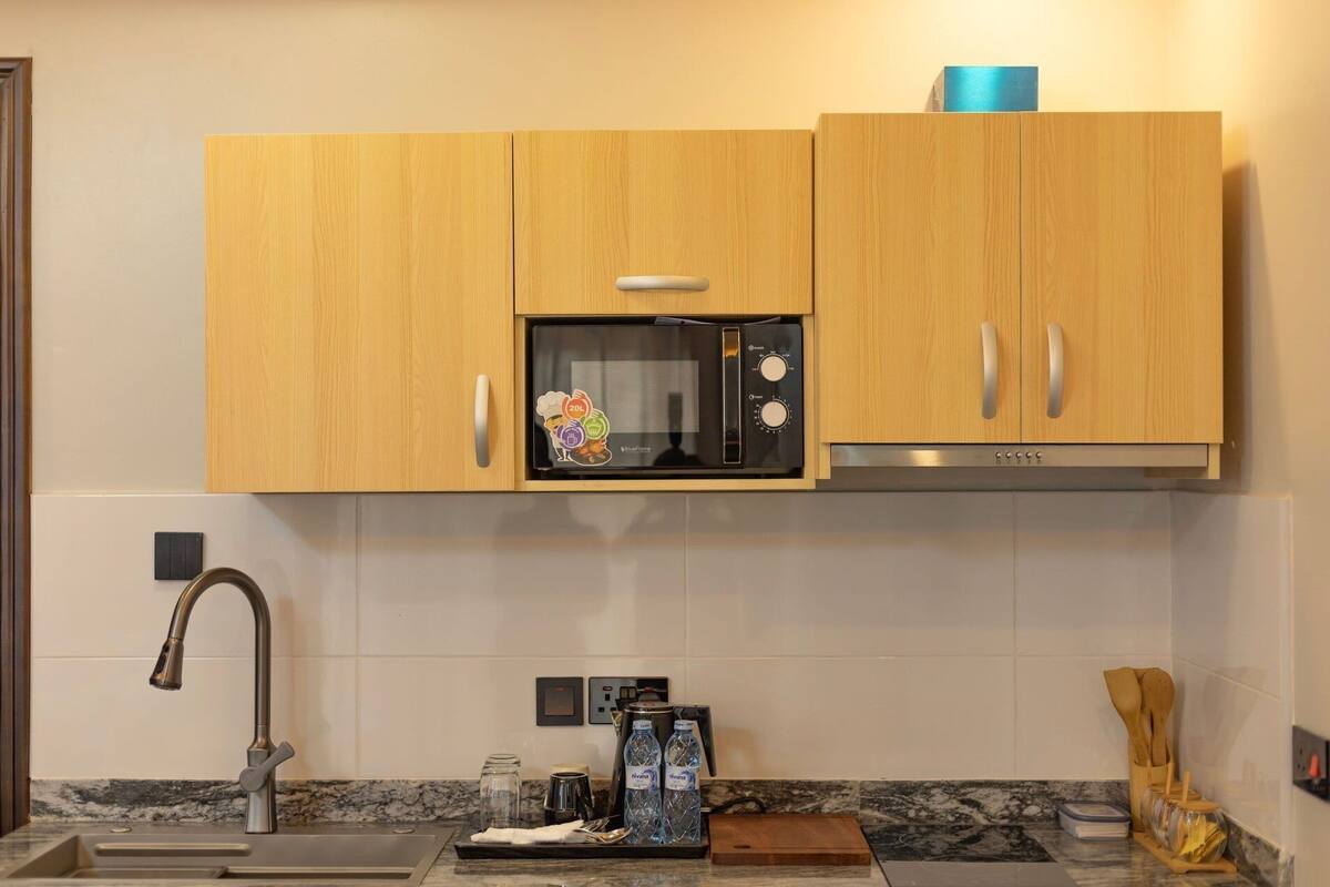 A kitchen with wooden cabinets, a microwave, a stainless steel sink, and a marble countertop.