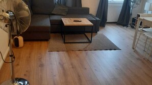 A living room with a sofa, a coffee table, a floor lamp, a standing fan, and a window with curtains. - Spacious 2BR 1LR Apartment Central Area (Vienna)