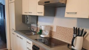 A compact kitchen with white cabinets, a stainless steel oven, a coffee maker, and a knife block on the countertop. - Spacious 2BR 1LR Apartment Central Area (Vienna)
