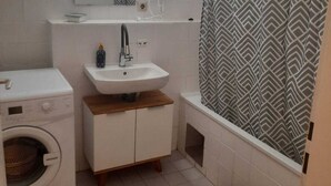 A compact bathroom with a washing machine, a sink, and a shower area. - Spacious 2BR 1LR Apartment Central Area (Vienna)