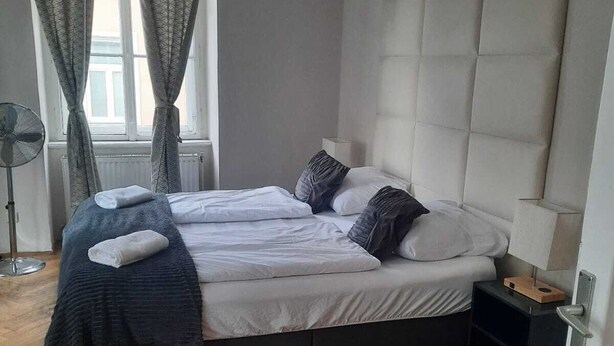 A bedroom with a bed, a bedside table, a floor lamp, and a window with curtains. - Spacious 2BR 1LR Apartment Central Area (Vienna)
