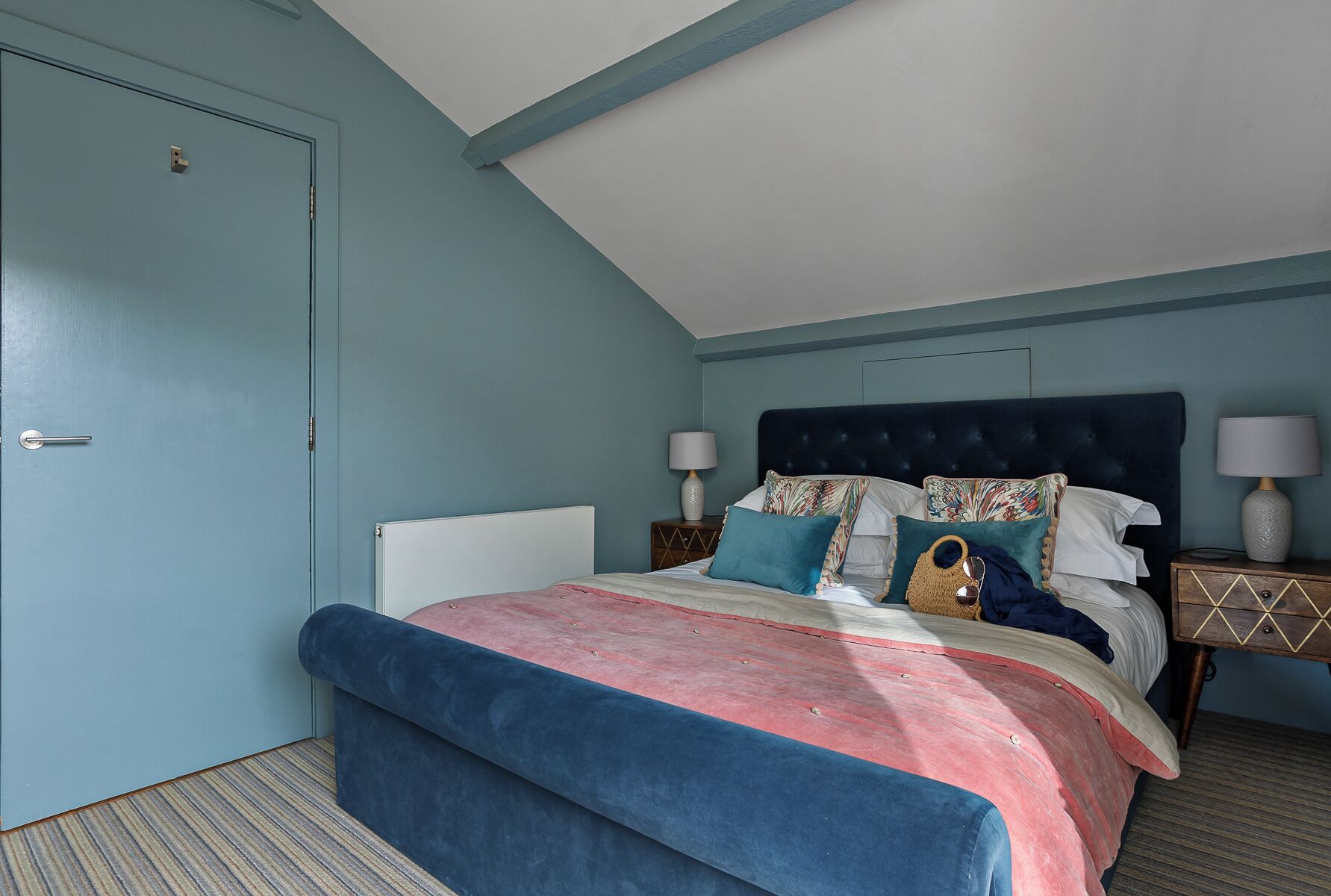 Un dormitorio con una cama, dos mesitas de noche y una puerta.
