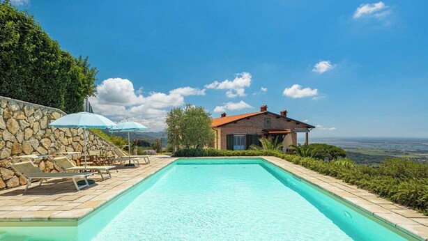 Ein Pool mit Liegestühlen und Sonnenschirmen, eine Steinmauer und ein Haus mit Blick auf die Landschaft.