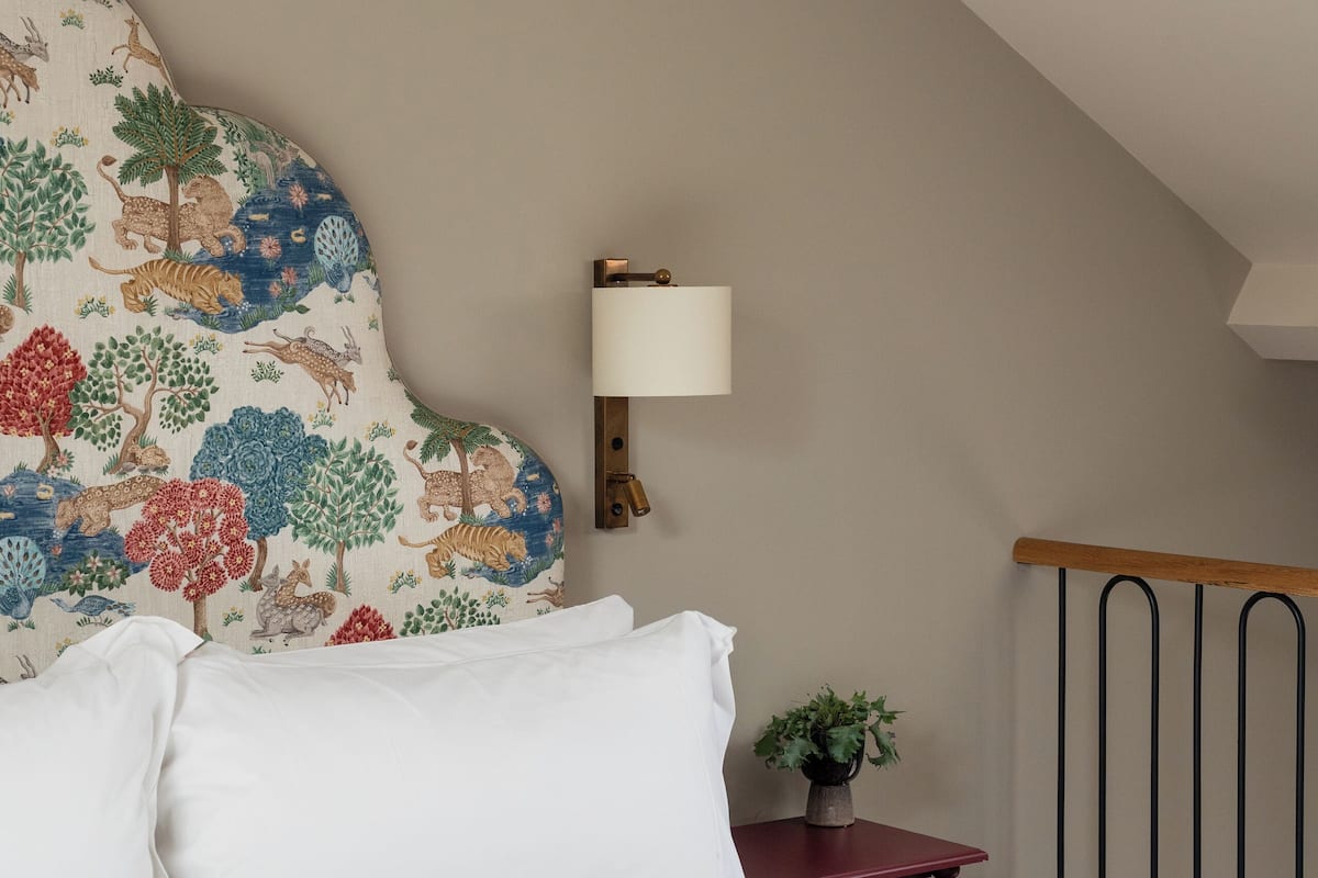 Un dormitorio con una cama grande, un cabecero decorativo, una mesita de noche con lámpara y vistas al exterior.