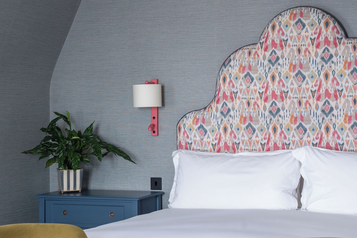 Una habitación de hotel con una cama, una mesita de noche, una lámpara, una planta en maceta y dos sillones.
