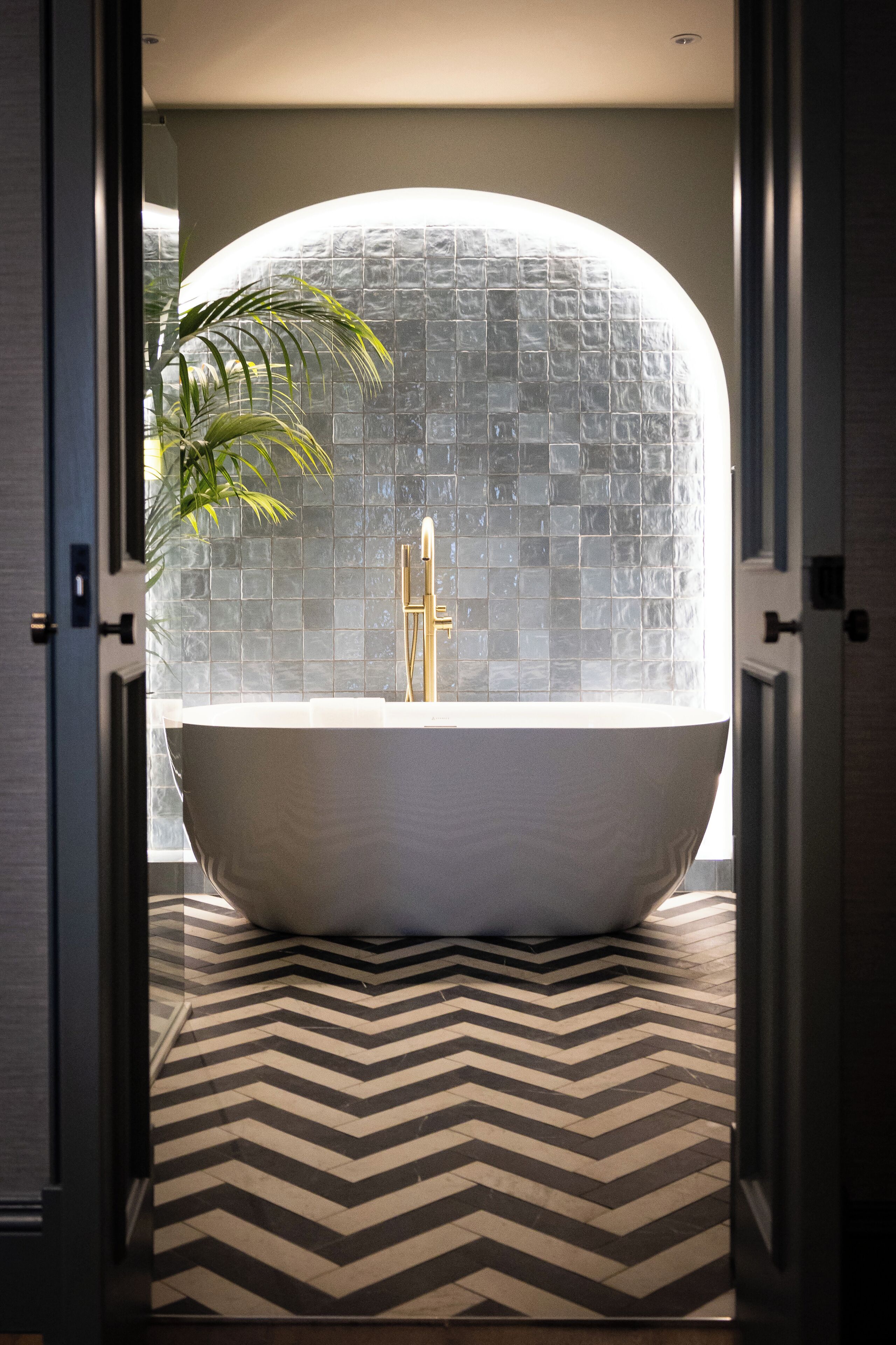 Un bagno moderno con una vasca freestanding, una parete piastrellata e un pavimento decorato.
