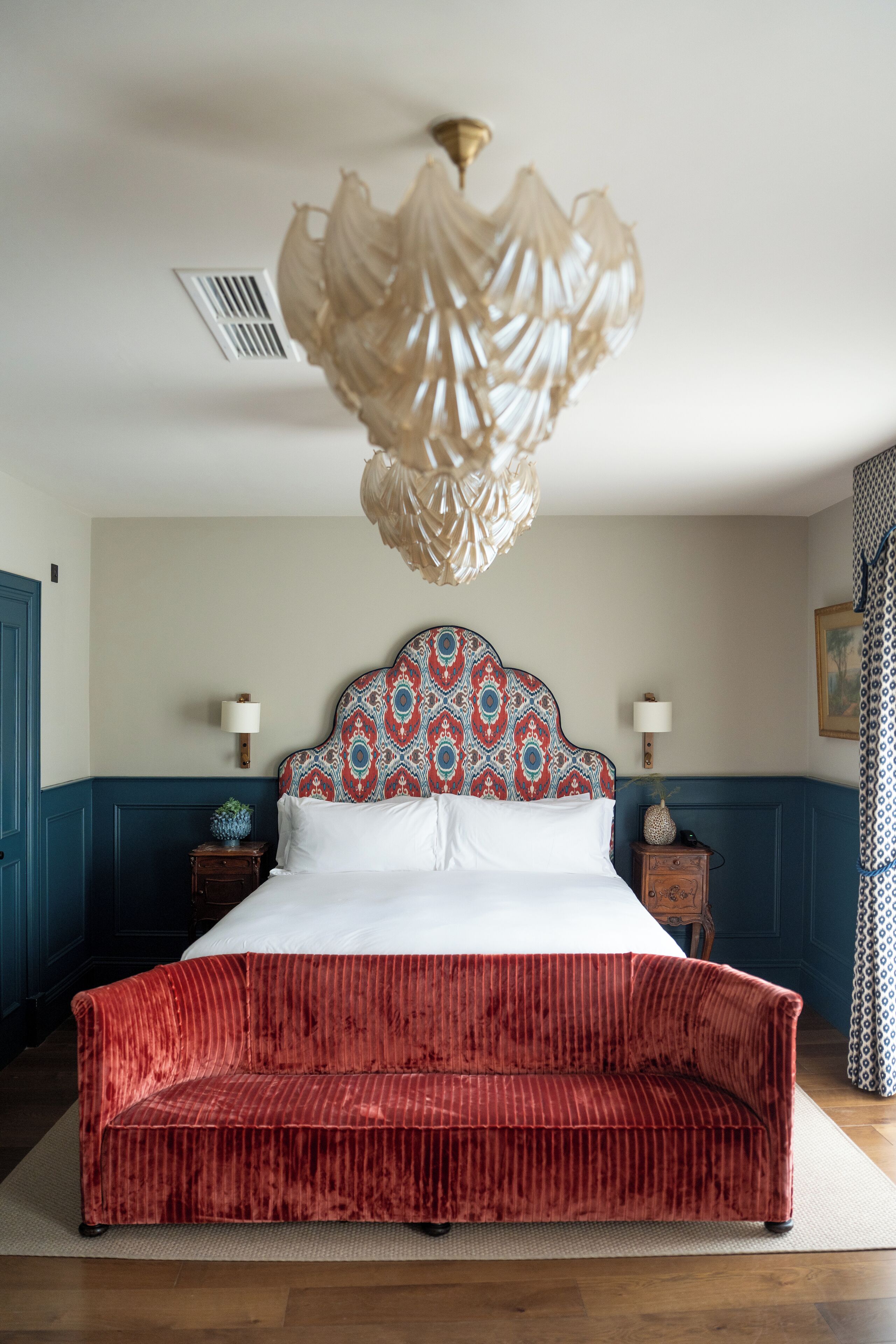 A bedroom with a large bed, a red sofa, a patterned headboard, and a hanging light fixture.