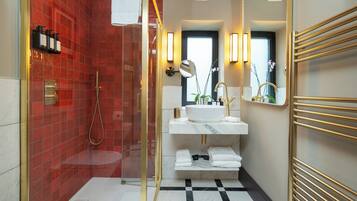 A modern bathroom with a red-tiled shower, a white sink with gold fixtures, and a black and white checkered floor.