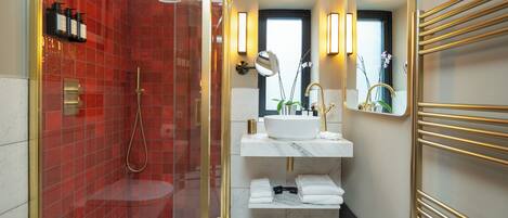 A modern bathroom with a red-tiled shower, a white sink with gold fixtures, and a black and white checkered floor.