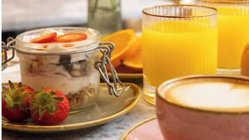 Un desayuno con un tarro de postre en capas, fresas frescas, un vaso de zumo de naranja y un bol de sopa sobre una mesa de mármol.