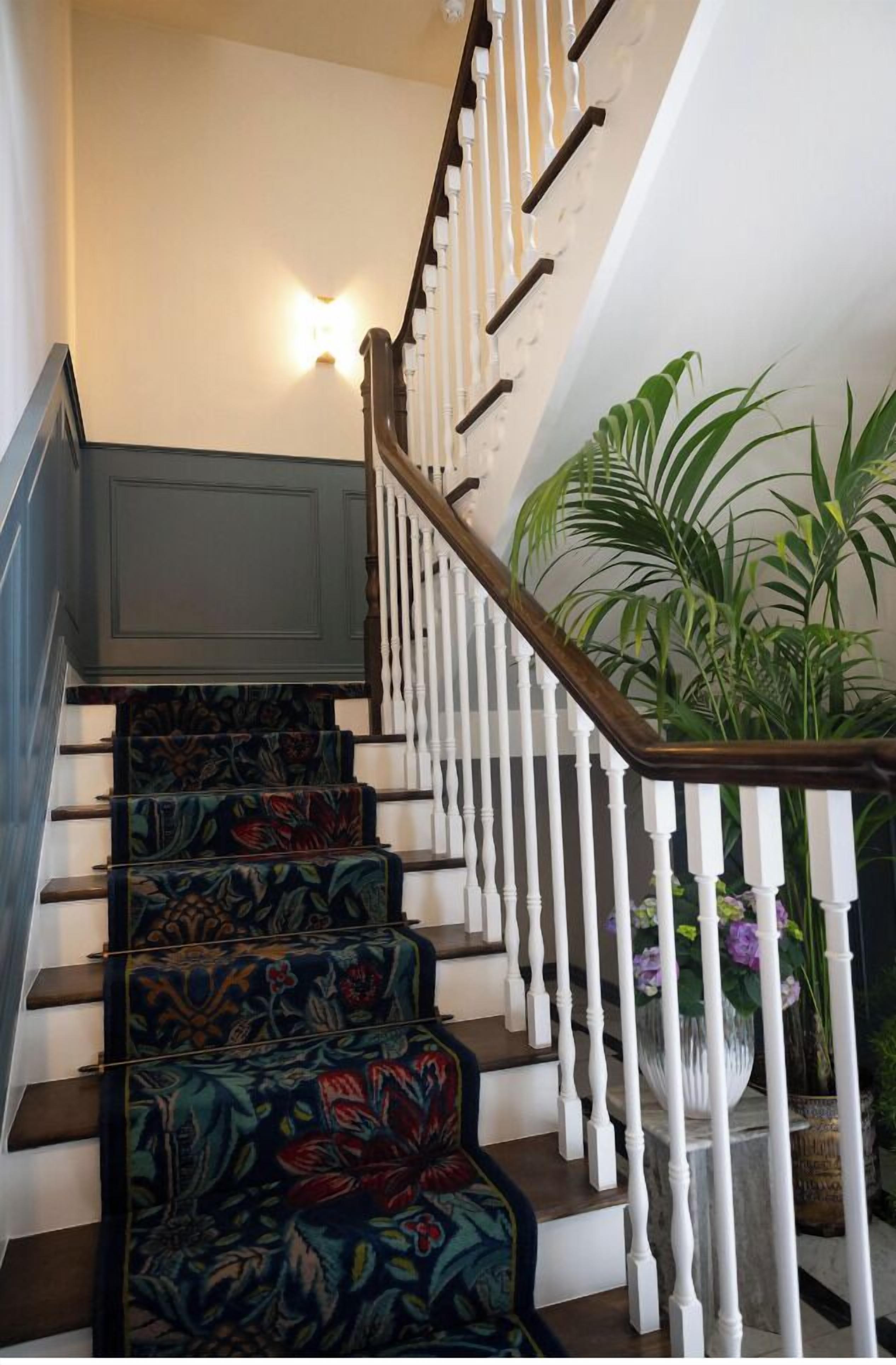 Un escalier orné de tapis à motifs floraux, de balustrades blanches et d’une plante en pot à sa base.