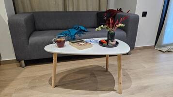 A modern living room with a grey sofa, a white coffee table with wooden legs, a book, a glass of tea, and a decorative vase with flowers.