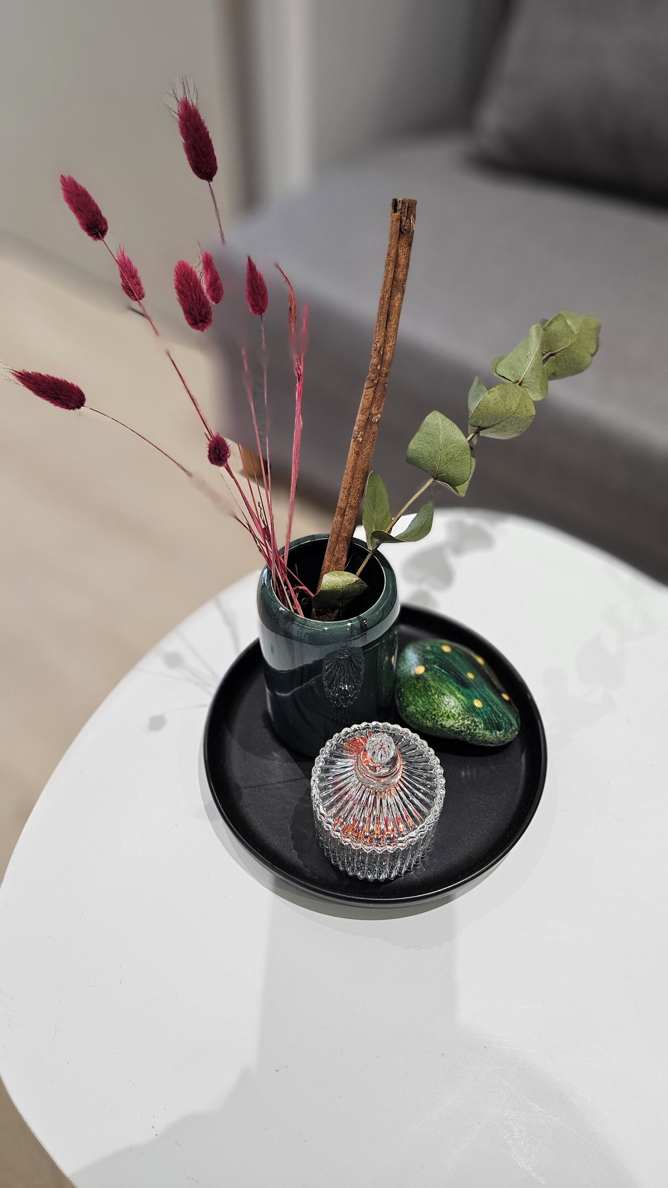 A small potted plant with a decorative glass container on a white table.