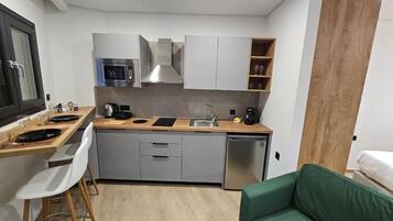 A compact kitchen with a microwave, stove, sink, and a dishwasher. There is a dining area with a table and chairs, and a green sofa in the corner.