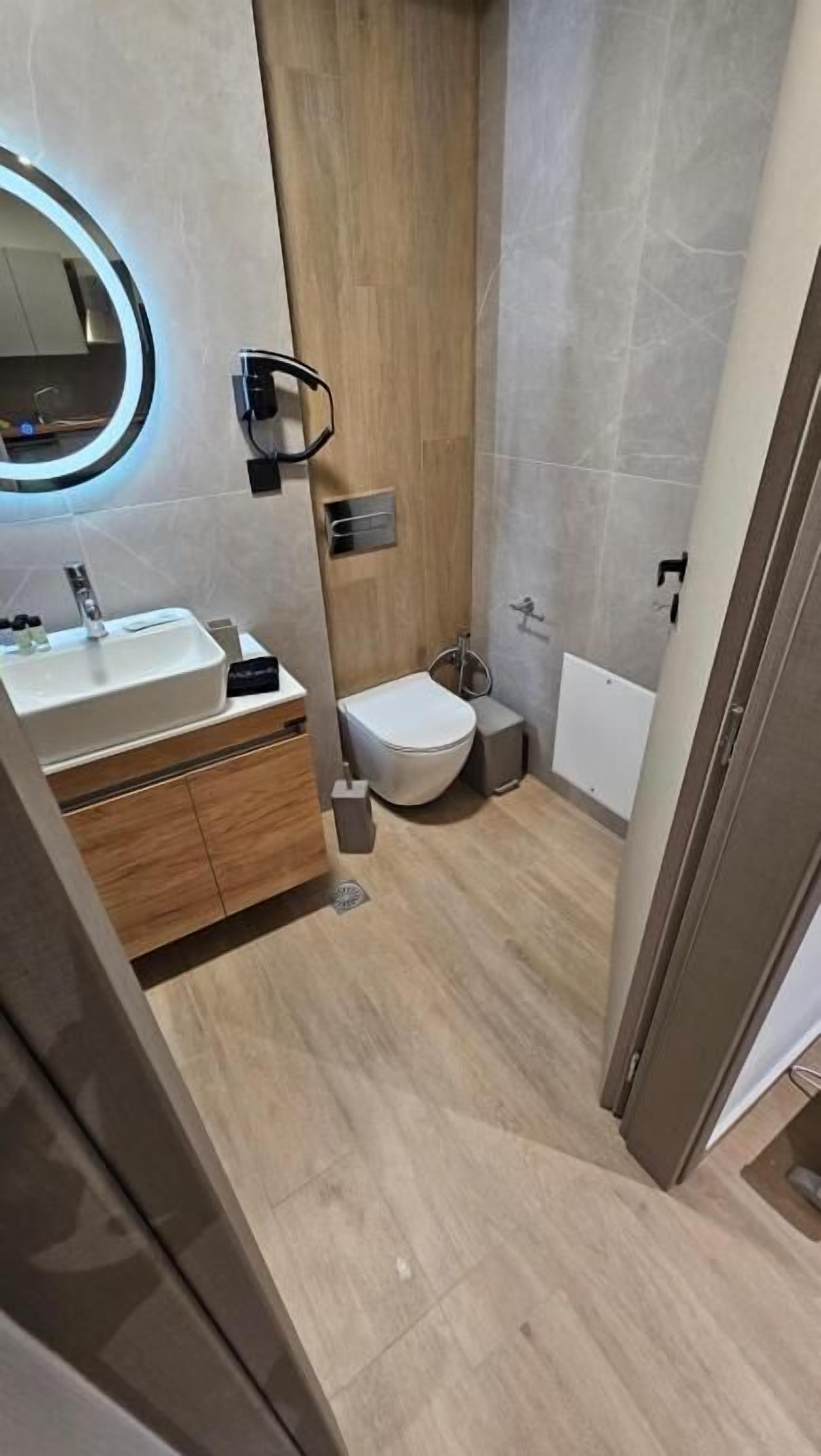 Une salle de bain moderne avec un meuble-lavabo en bois, un miroir rond, des toilettes et un espace douche.