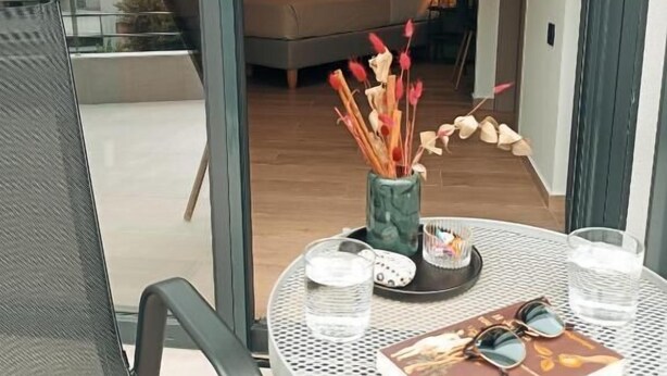 Une chambre moderne avec un lit, une table à manger avec des verres et un livre, et un balcon offrant une vue.