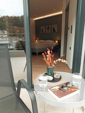 A modern room with a bed, a dining table with glasses and a book, and a balcony with a view. - Sezame (Ioannina)