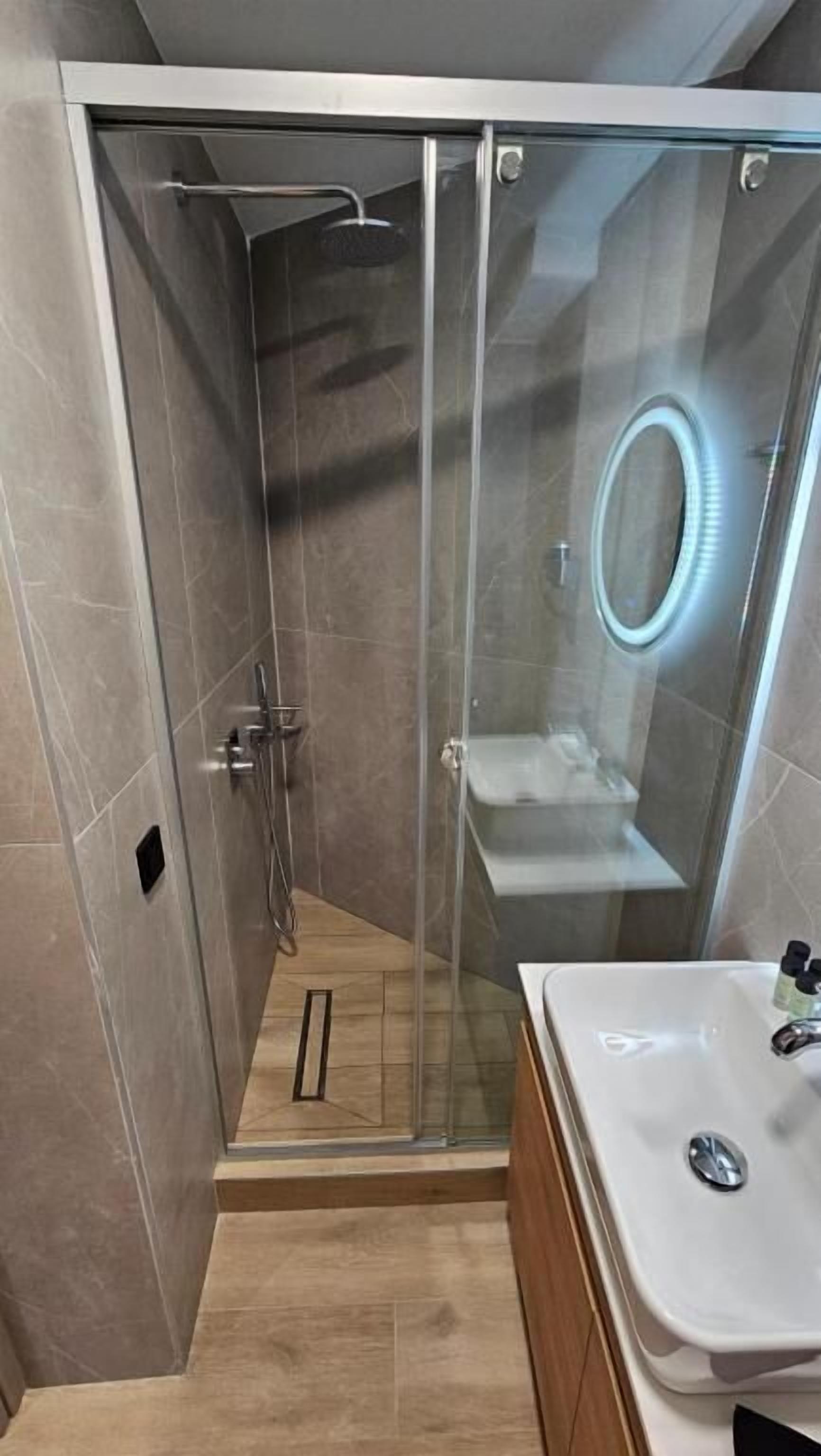 A modern bathroom with a glass-enclosed shower, a white sink, and a wooden vanity.