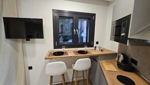Une petite cuisine avec une fenêtre, un four à micro-ondes et deux chaises blanches.