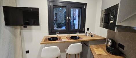 A compact kitchen with a window, a microwave, and two white chairs.