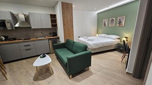 A compact room with a kitchenette, a bed, a green sofa, and a small table. - Sezame (Ioannina)