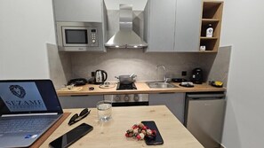 A compact kitchen with a microwave, stove, sink, and a laptop on the counter. - Sezame (Ioannina)