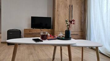 A modern room with a wooden cabinet, a flat-screen TV, a table with a glass of tea, a smartphone, and a decorative vase.