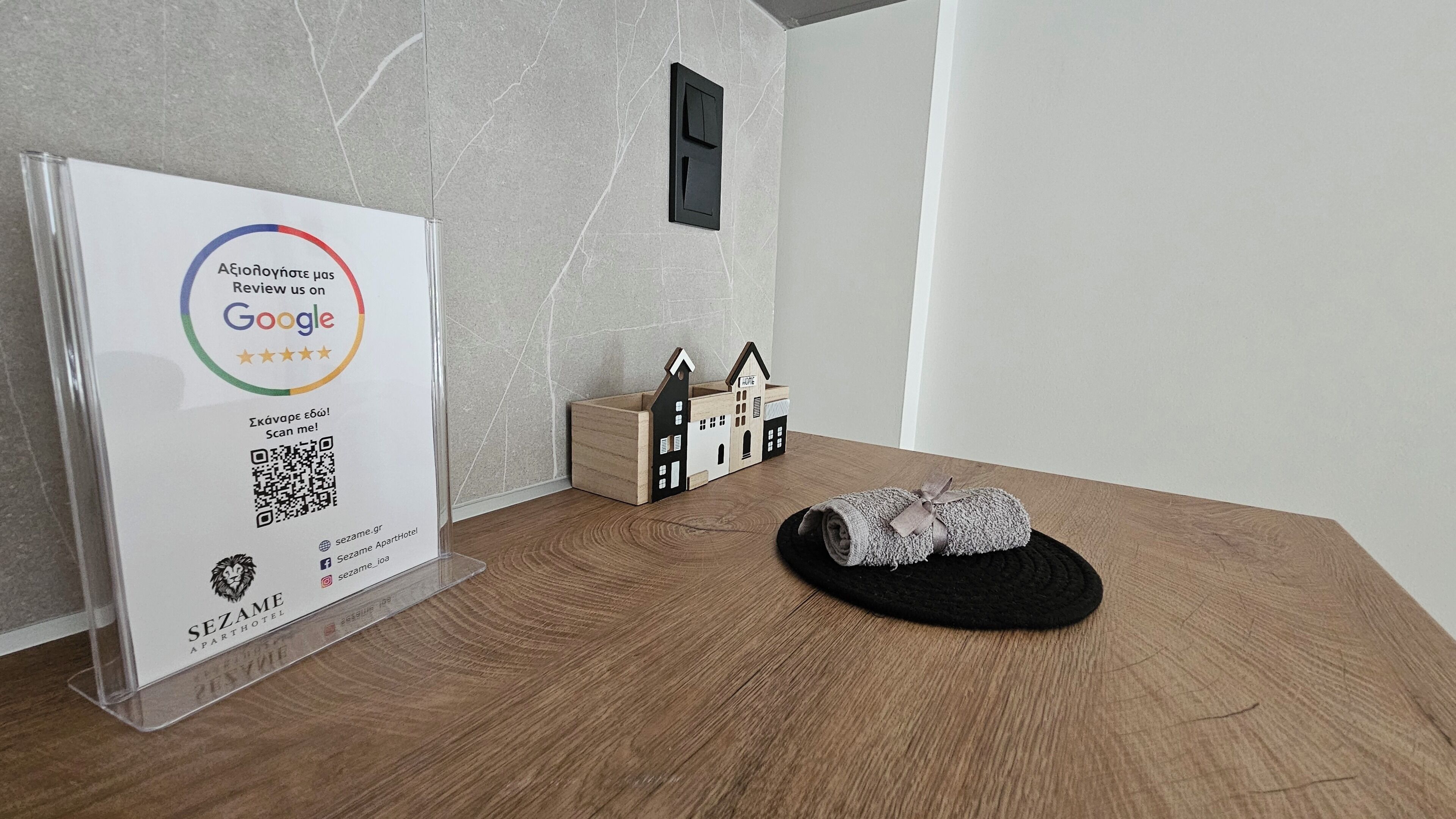Een houten tafel met een bord voor een Google-recensie, een klein modelhuis en een opgerolde handdoek.
