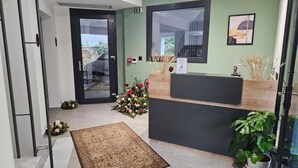 Un espace d’accueil comprenant un comptoir de réception, un petit tapis, une plante en pot et un arrangement floral.