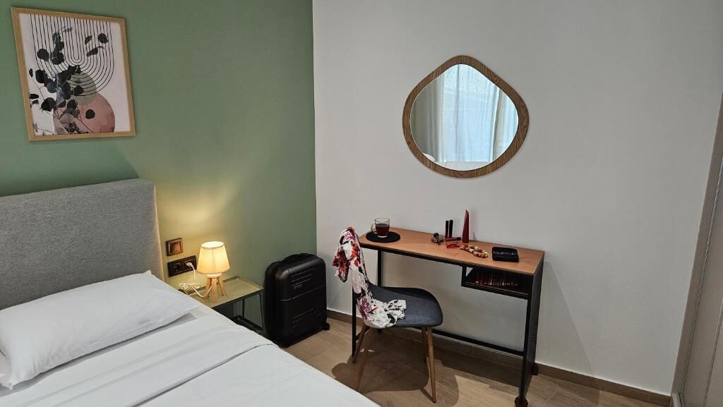 Una habitación de hotel con cama, escritorio, silla, lámpara y espejo.