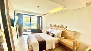 A hotel room with a large bed, a wooden nightstand, a chair, and a view of the outdoors through a sliding door. - Horison Kuta Bali (Kuta)