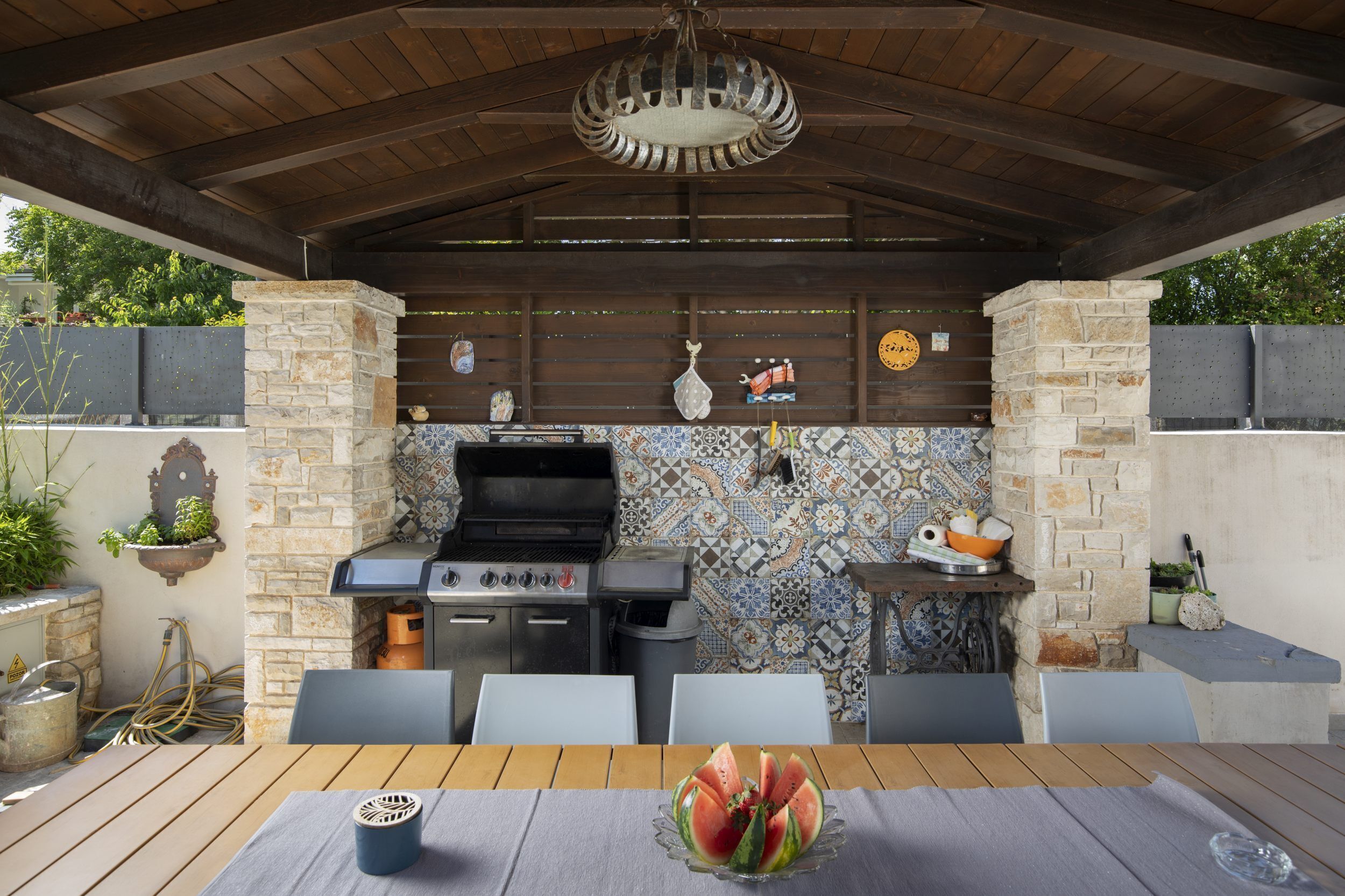 Cucina esterna con barbecue, zoccolo a mosaico e tavolo da pranzo con sedie.