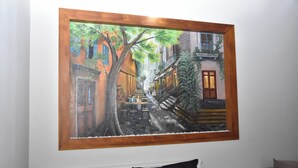 Un cuadro enmarco que muestra una calle estrecha flanqueada por edificios, un árbol en el centro y una escalera que conduce a un nivel superior.