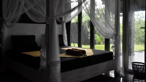 Una cama con dosel, vistas a un jardín a través de amplios ventanales y una cesta en el suelo.
