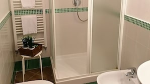 Une salle de bain avec douche, deux toilettes et un bidet.