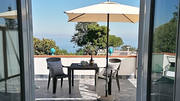 Une terrasse avec une table et des chaises, un grand parasol et une vue sur la mer.