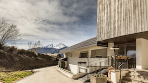 A modern building with a staircase leading to a balcony, surrounded by a landscaped garden and a mountain view. - Vacation apartment Bergkristall with Watzmann view (Berchtesgaden)