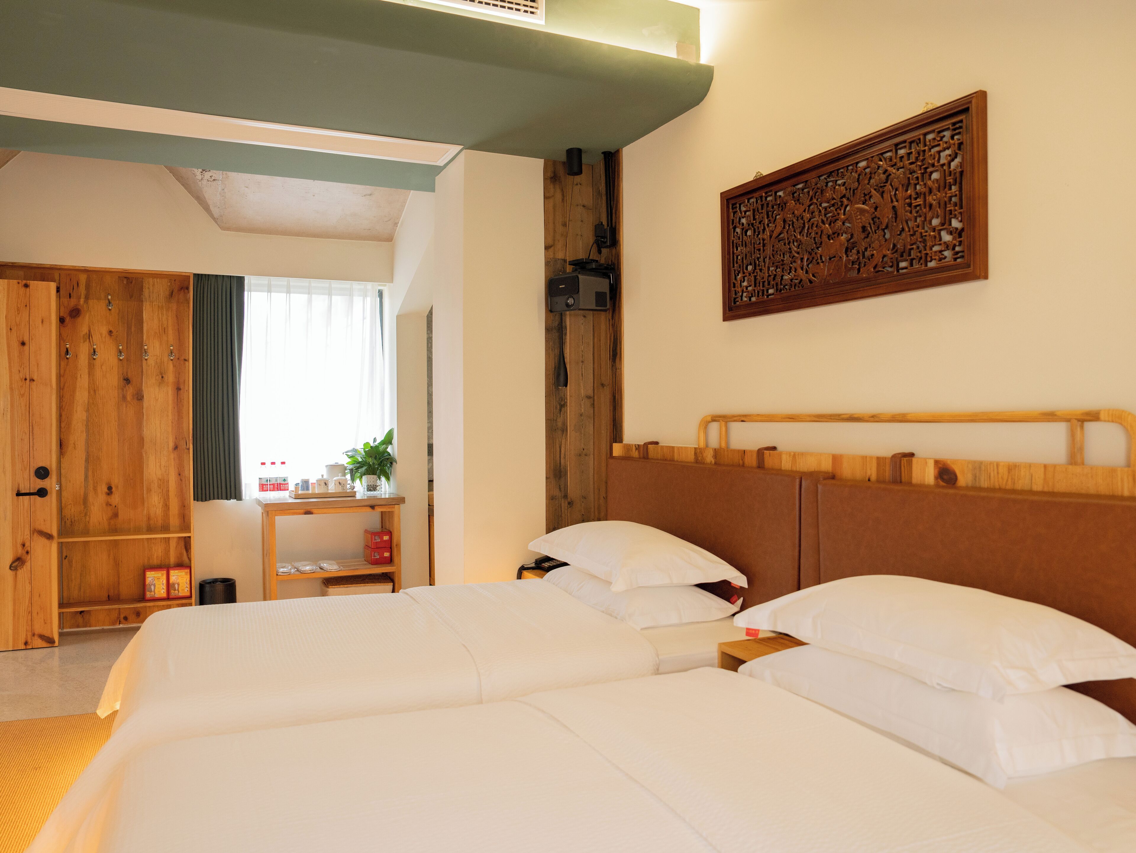 A hotel room with a large bed, a wooden wardrobe, a small table with a plant, and a decorative wooden panel on the wall.