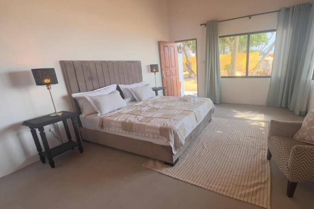 A bedroom with a bed, a nightstand, a chair, and a window with curtains.