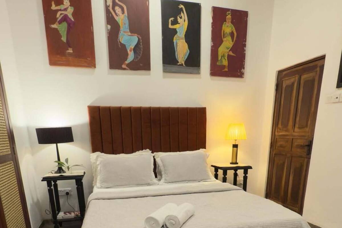 A neatly made bed with white linens, two bedside tables with lamps, and three wall-mounted paintings of dancers.