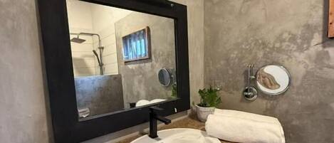 A bathroom with a granite countertop, a white sink, a large mirror, a potted plant, and a towel rack.