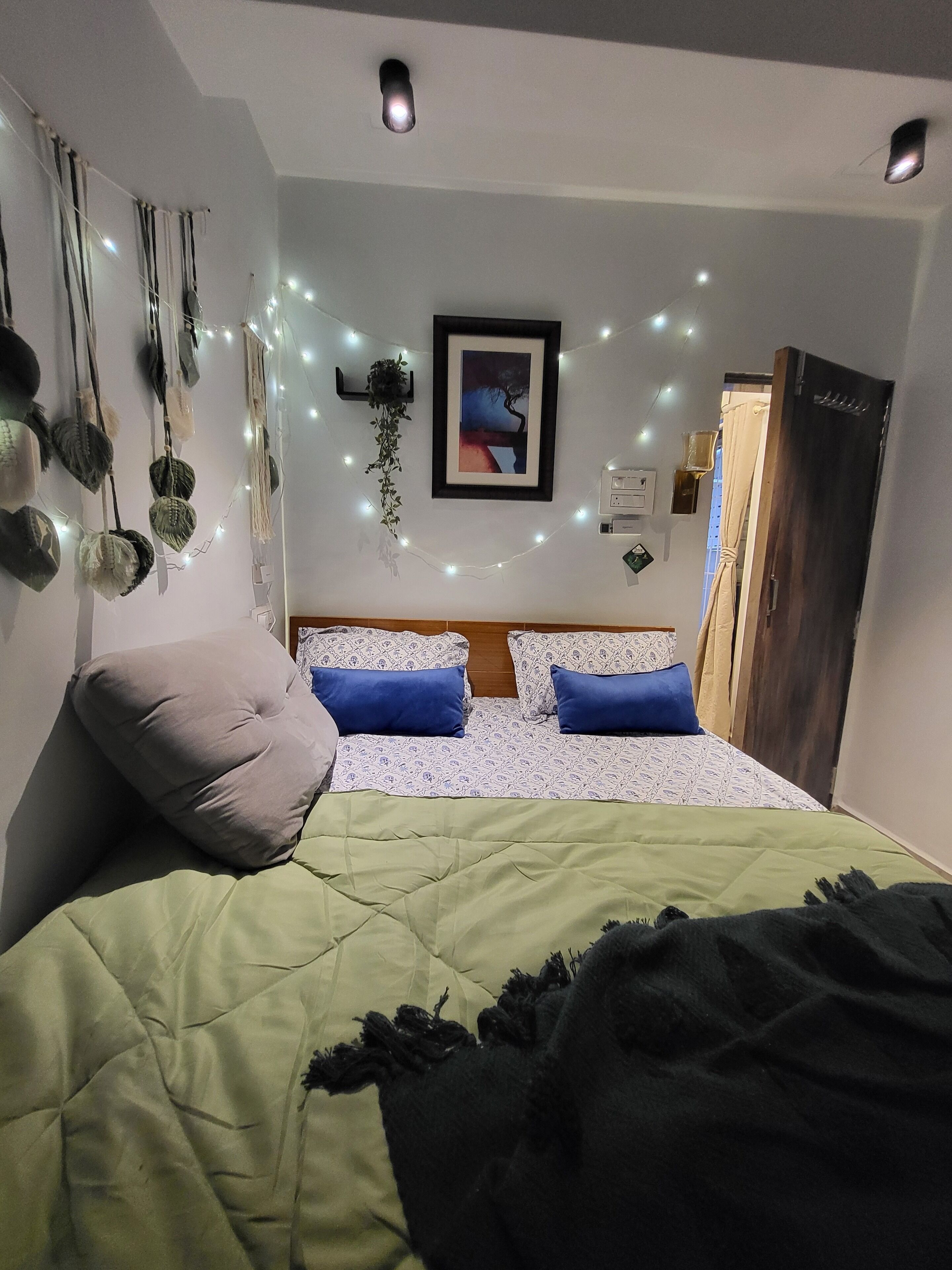 A bedroom with a bed, pillows, a framed picture, and string lights.