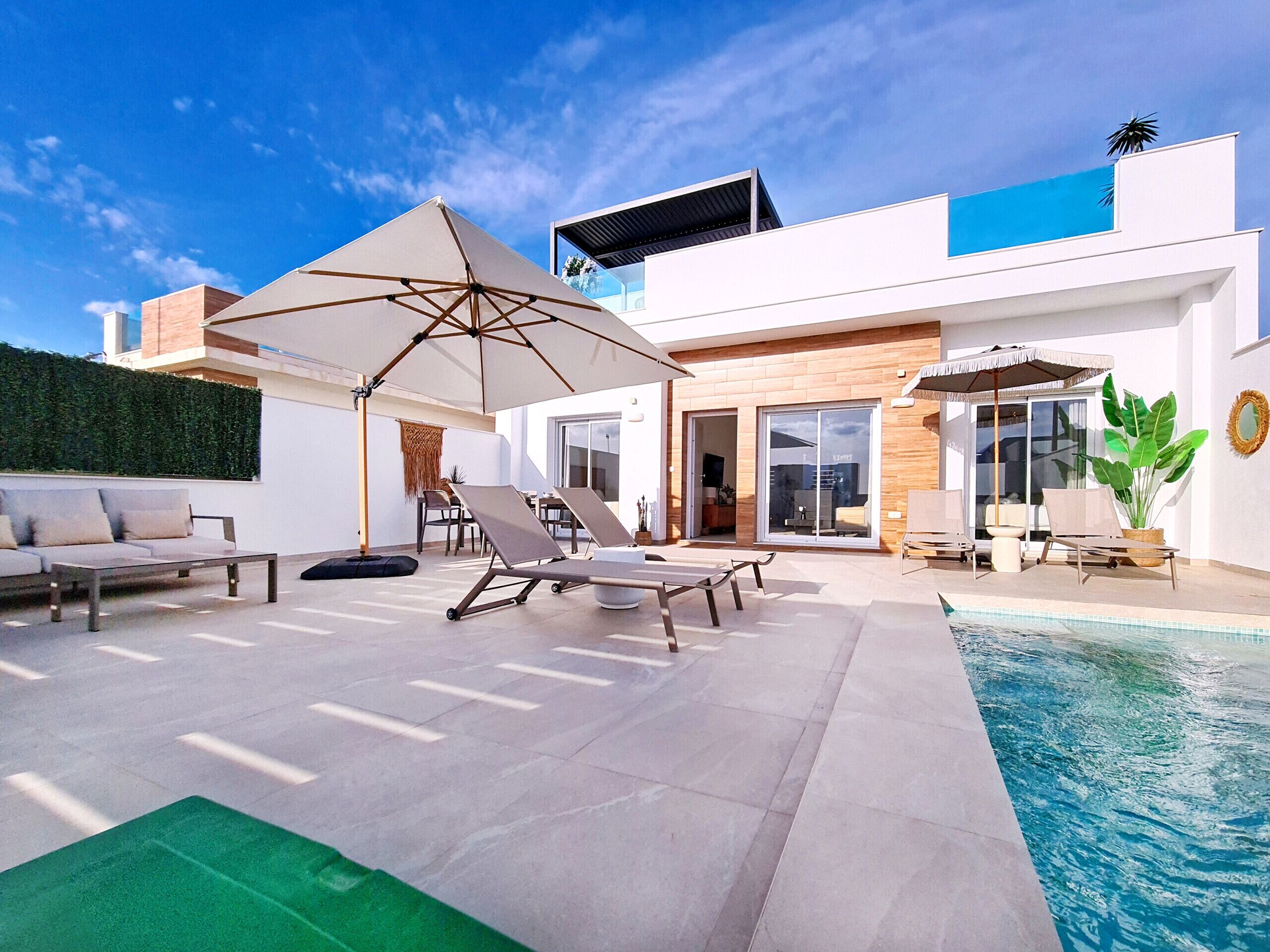 A modern outdoor pool area with lounge chairs, a large umbrella, and a glass-enclosed patio.