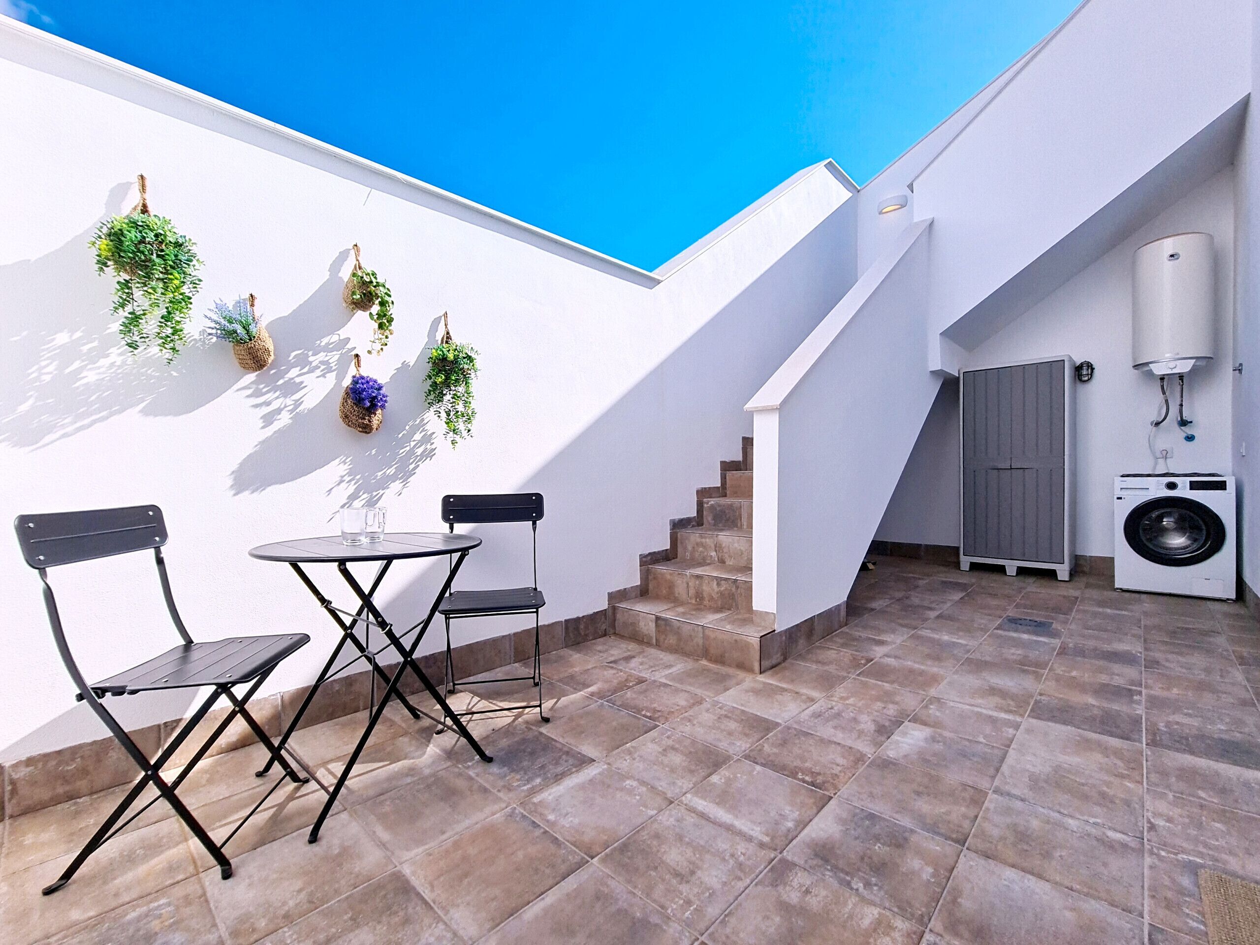 Une petite terrasse extérieure avec une table et des chaises, un lave-linge et un escalier.