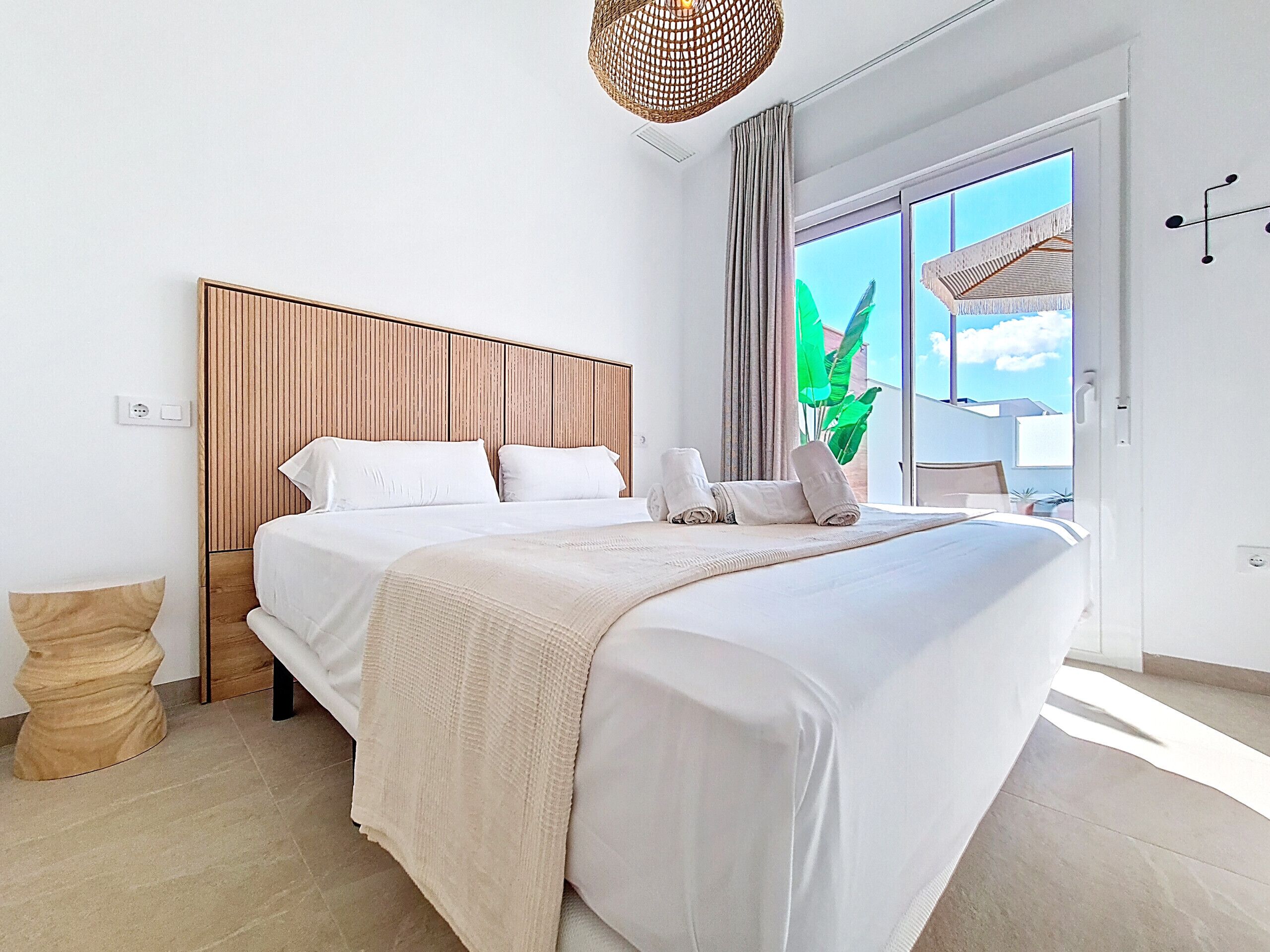 Une chambre moderne avec un grand lit, une tête de lit en bois et une vue sur la verdure.