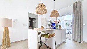 Cozinha moderna com ilha central, banquetas, luminárias pendentes de vime e vista para o exterior através de uma grande janela.